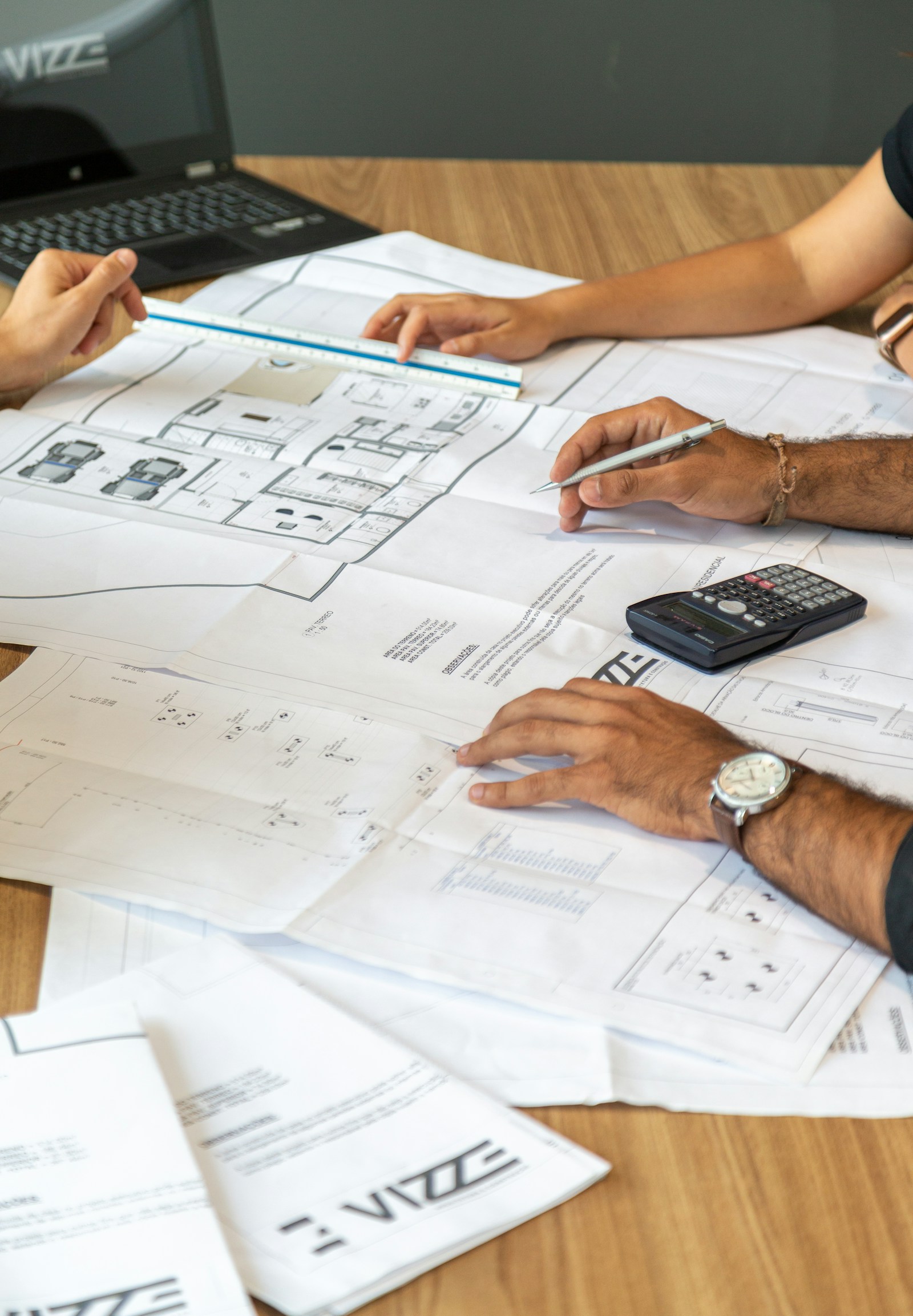 Architects reviewing building plans on a desk with a calculator, ruler and pencil
