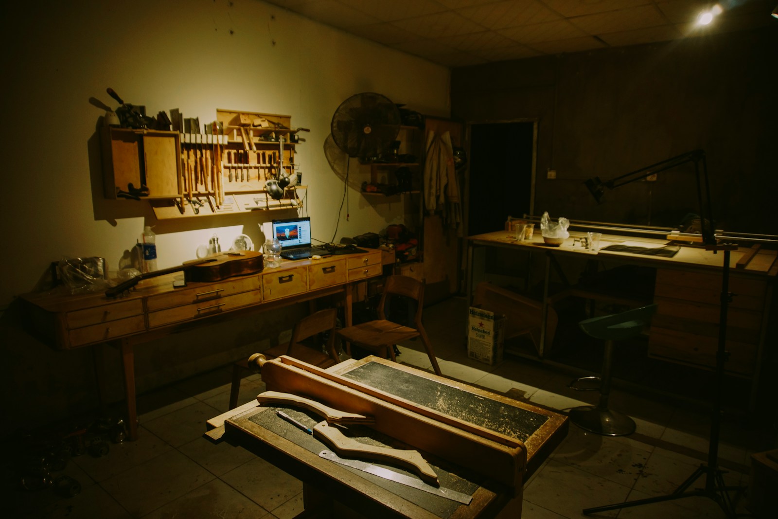 A warmly lit craftsman's workshop with hand tools on the wall and a laptop on the bench